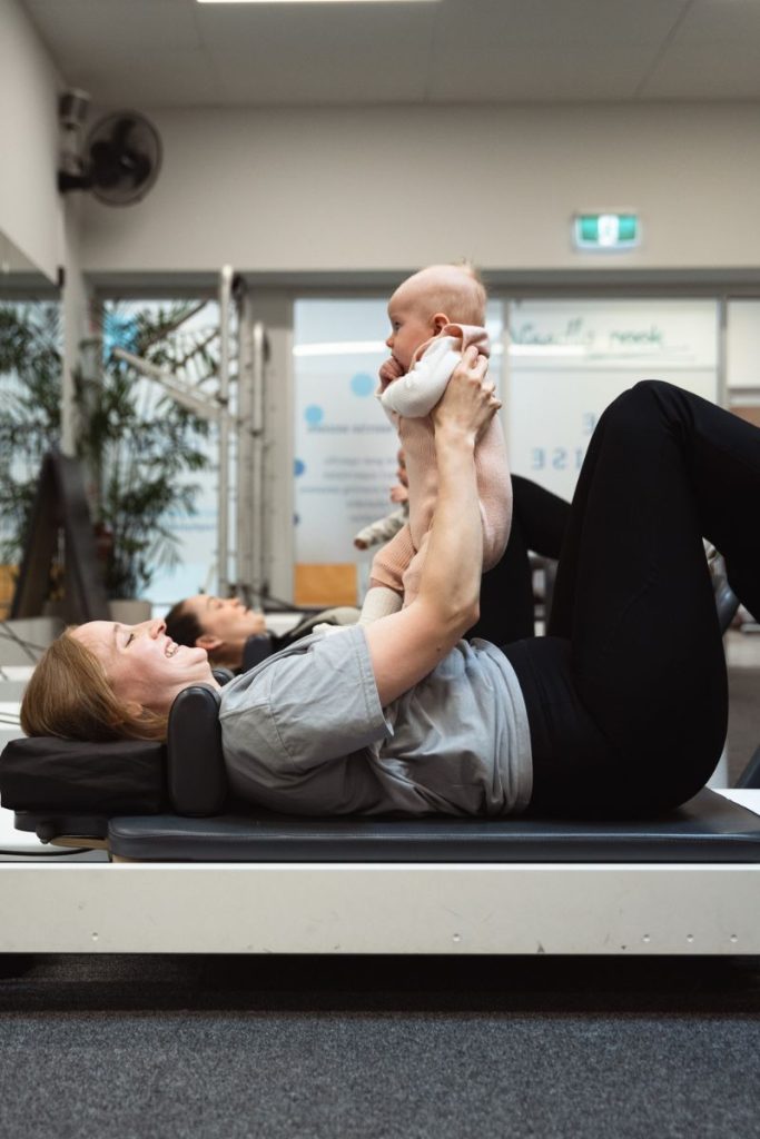 Two new mums and their babies perform a pilates exercise holding their baby