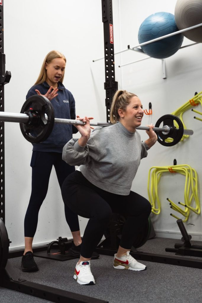 A Pregnant lady performs a barbell squat under the guidance of Pregnancy Physiotherapist sophie