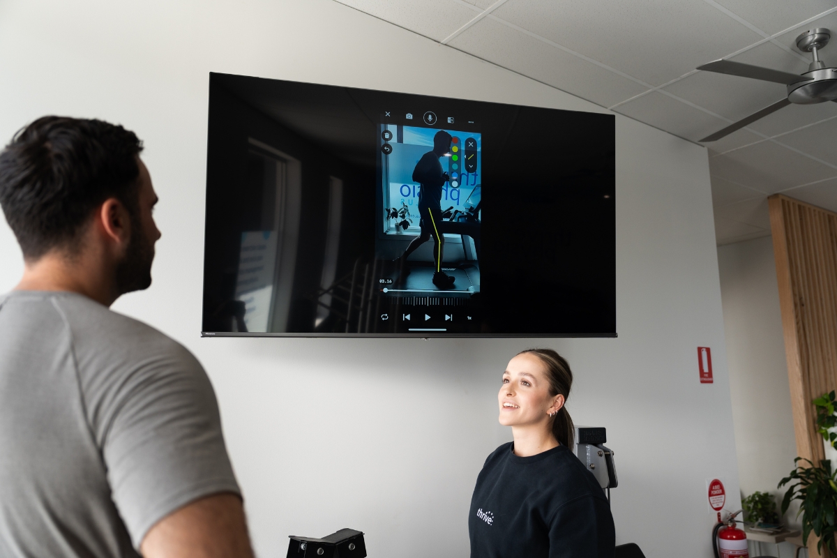 Running physio explains the findings of a running gait analysis using a big screen TV to running form
