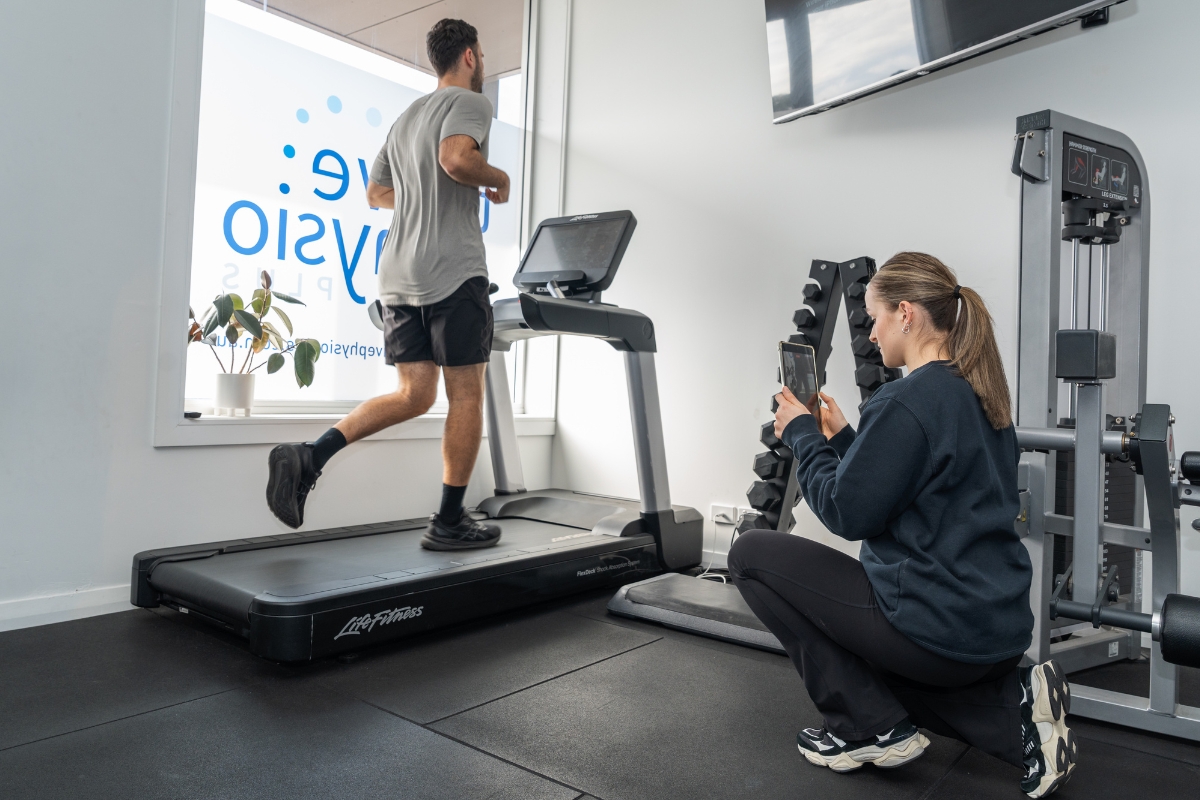 Client on a treadmill running undertaking a running gait assessment is filmed by a running physio as part of a running assessment